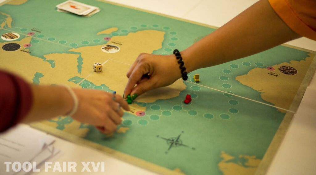 Close-up of an educational game about migration. Two hands move pieces on a colored board.